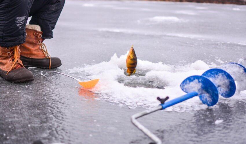 A man is standing on an ice pond with a fishing pole.