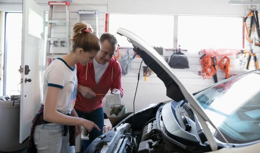 A man and woman looking at the hood of a car.