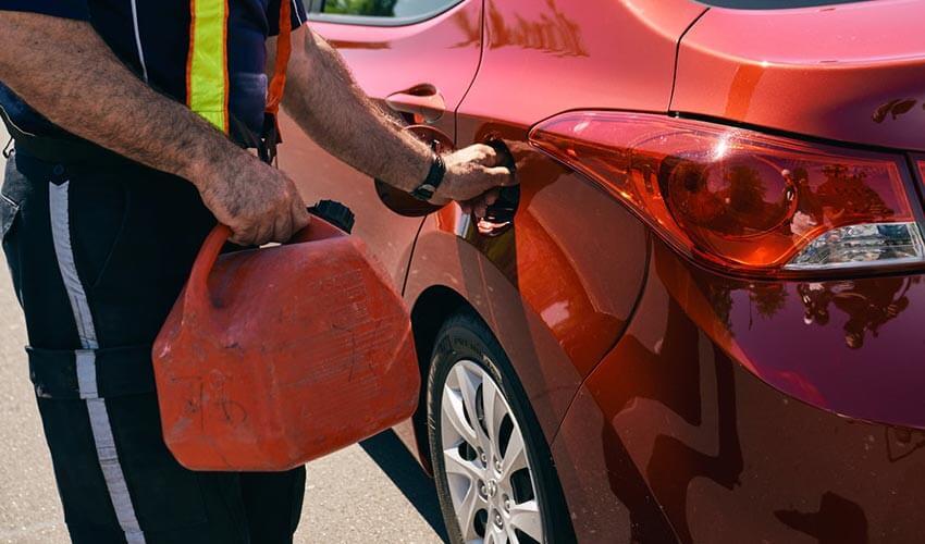A man filling up a red car with gas.