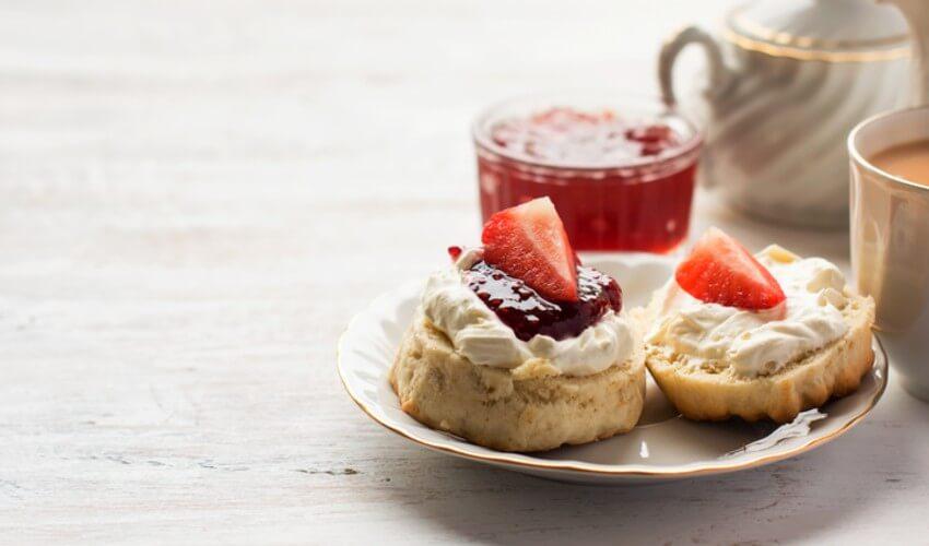 Scones with jam and cream on a plate next to a cup of tea.