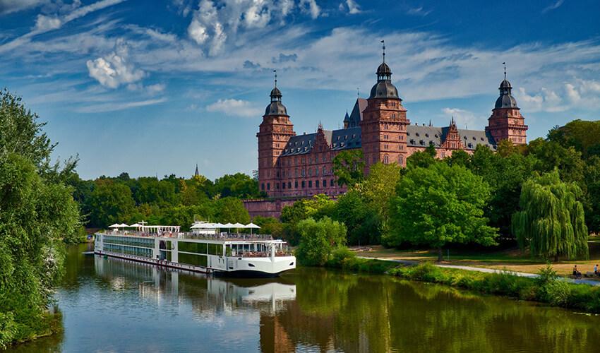A boat is traveling down a river with a castle in the background.