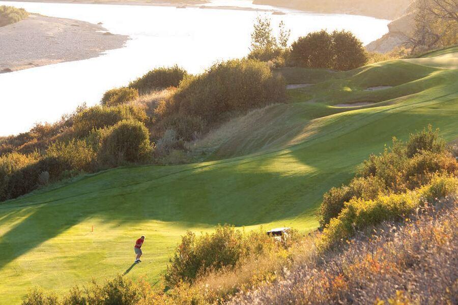 A golfer walking on a course near a water body during sunset.
