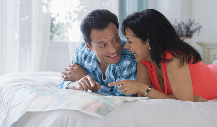 A man and woman laying on a bed looking at a map.