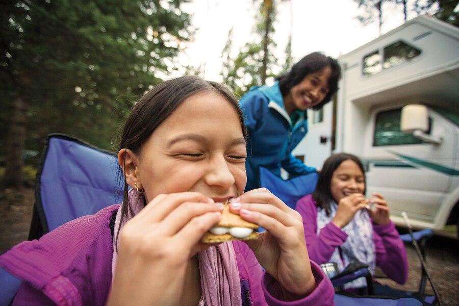 A group of girls eating a hamburger in front of an rv.