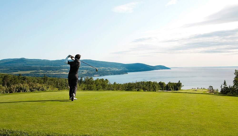 A man is playing golf on a golf course overlooking the ocean.