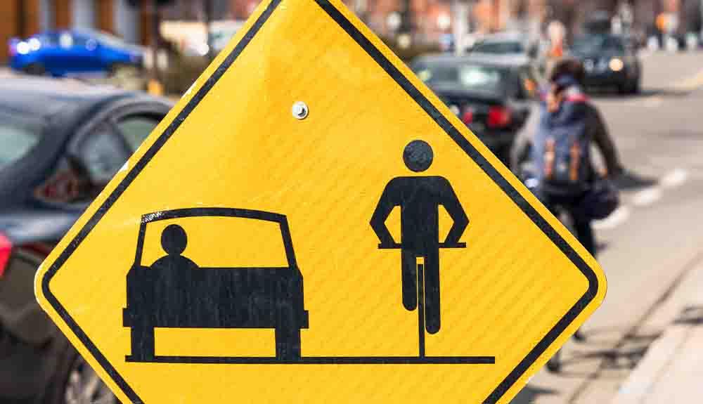 A yellow sign with a man riding a bike in front of a car.
