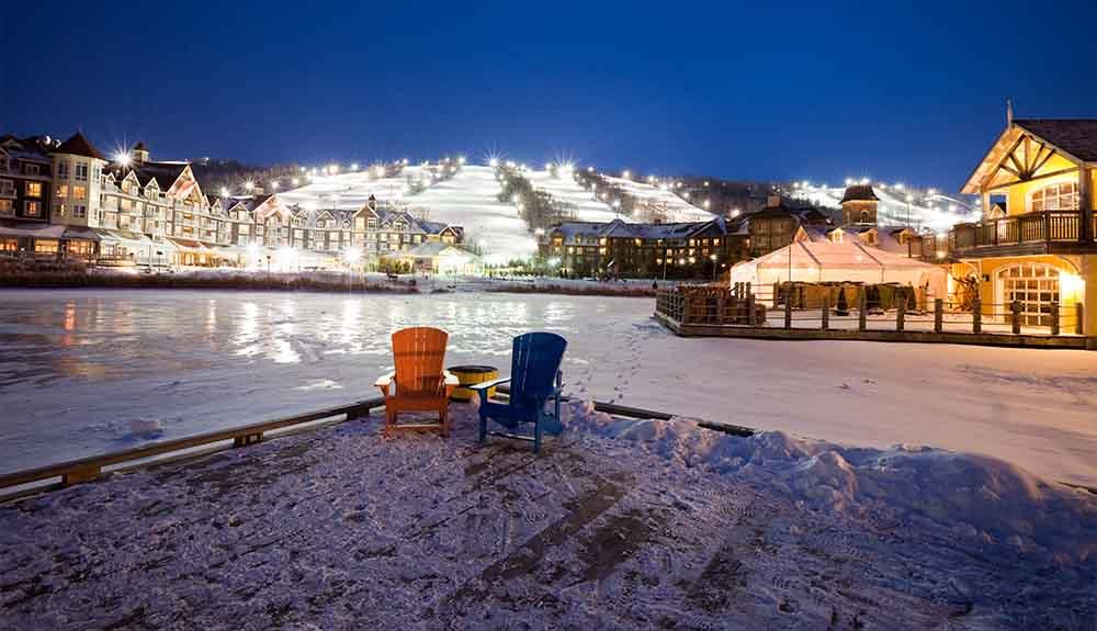 Chairs on a dock with a lake and buildings in the background.