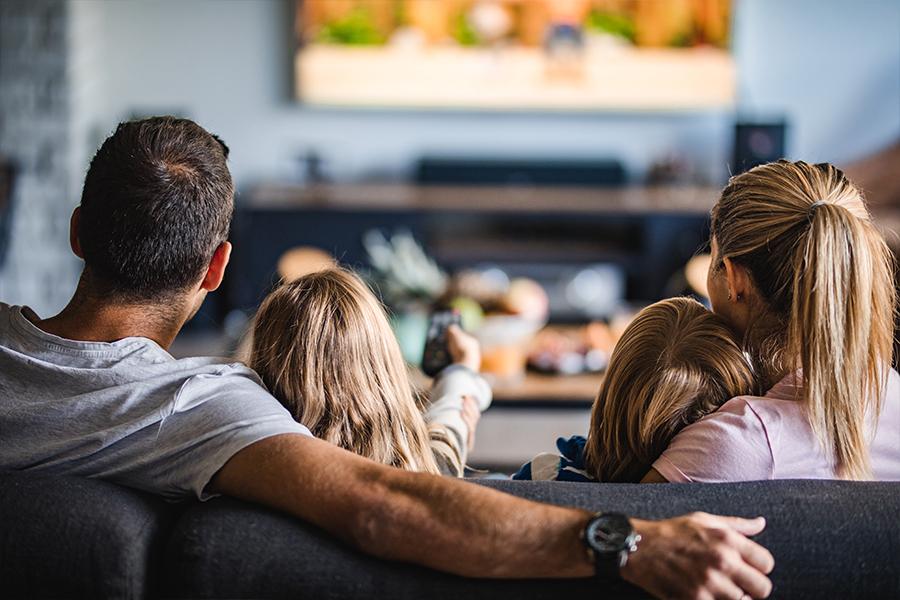 A family sitting on a couch watching television.