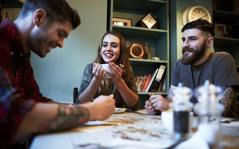 Three people gathered around a table, one is drinking coffee.