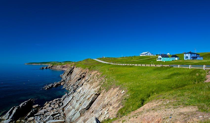 A blue house sits on a cliff overlooking the ocean.