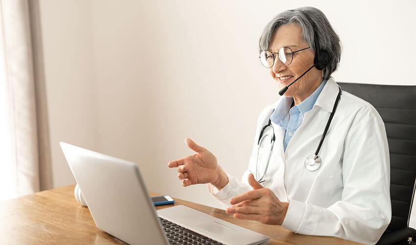 A woman in a lab coat is talking on a laptop.