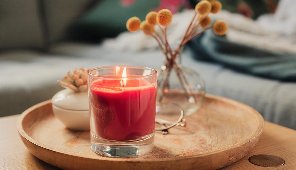 A red candle sits on a wooden tray in front of a couch.