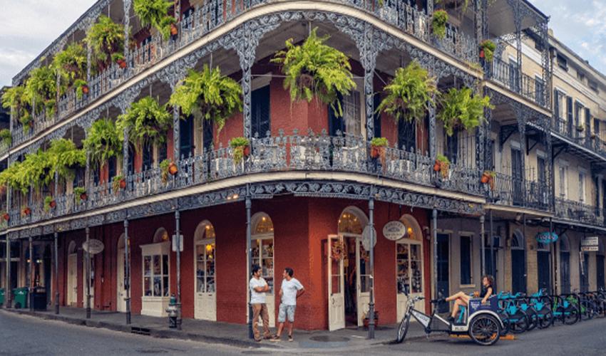 Iron-balconied building in the french quarter of new orleans with pedestrians and a pedicab.