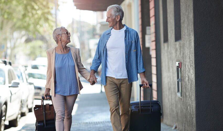 An older couple walking down the street with luggage.