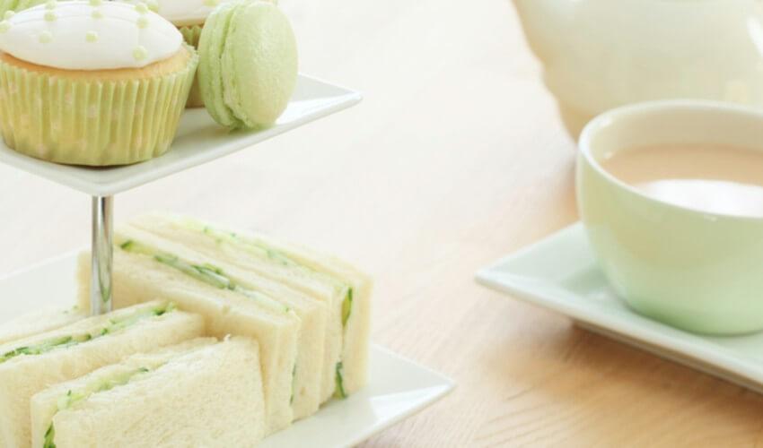 A plate with sandwiches, cupcakes and a cup of tea.