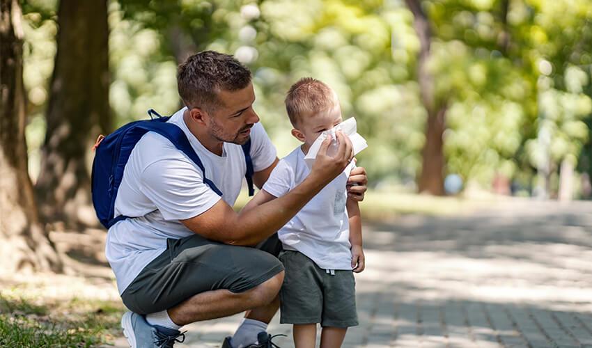 A man is holding a child's hand and blowing his nose.