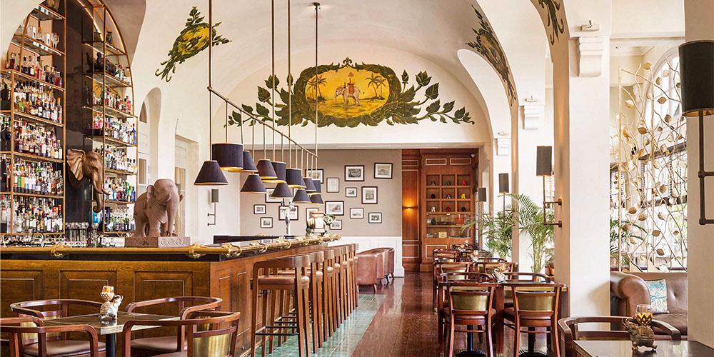 Elegant bar with a classic wooden counter, mounted wall art, and decorative hanging lamps.