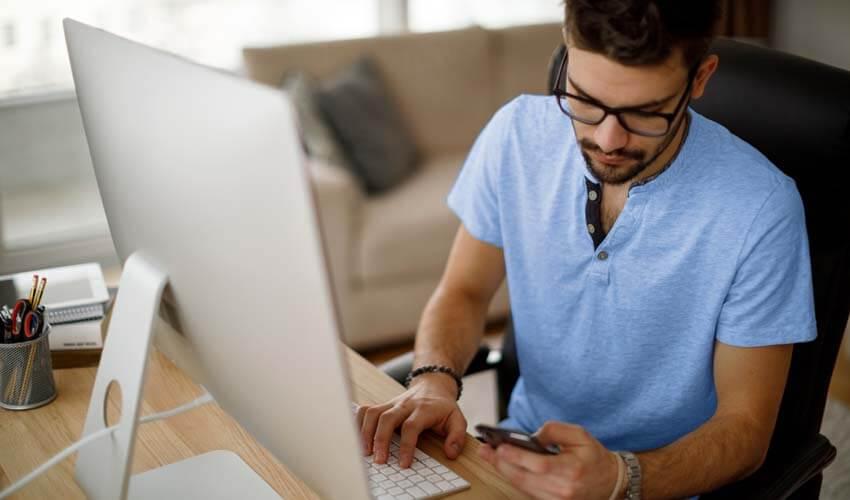 A man using a cell phone while sitting at a desk.