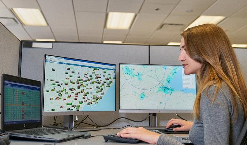 A woman working on a computer with two monitors.