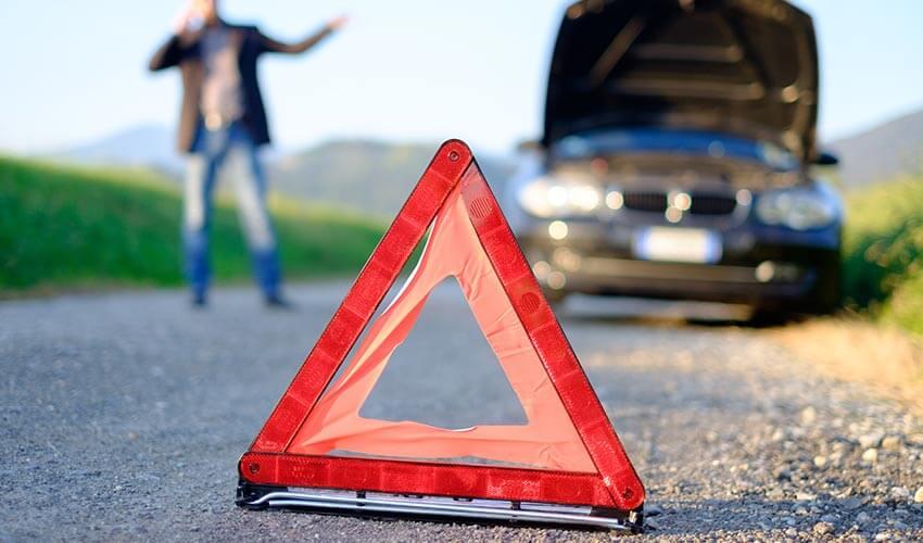 A man standing next to a broken car on a road.