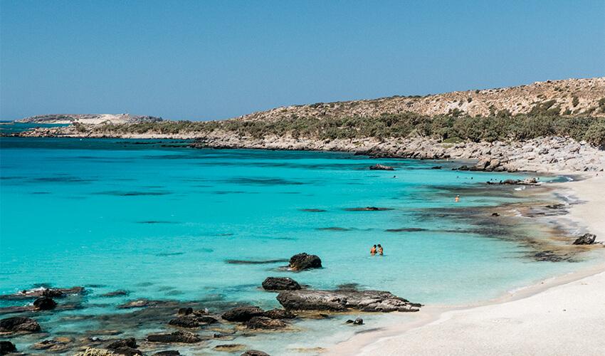 A beach with clear blue water and rocky cliffs.