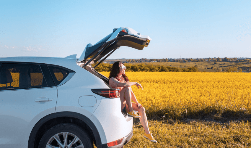 A woman sitting in the trunk of a suv in a field.
