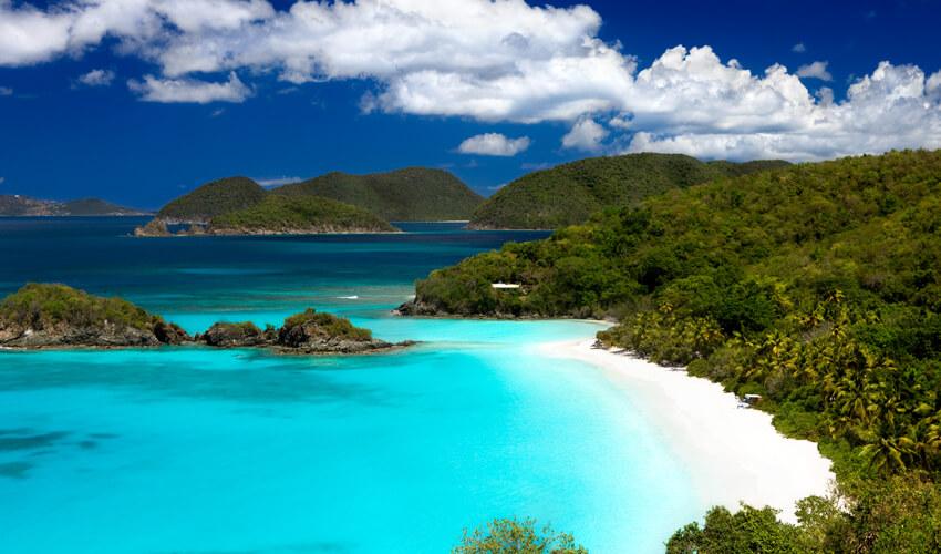 A beach with turquoise water and green trees.