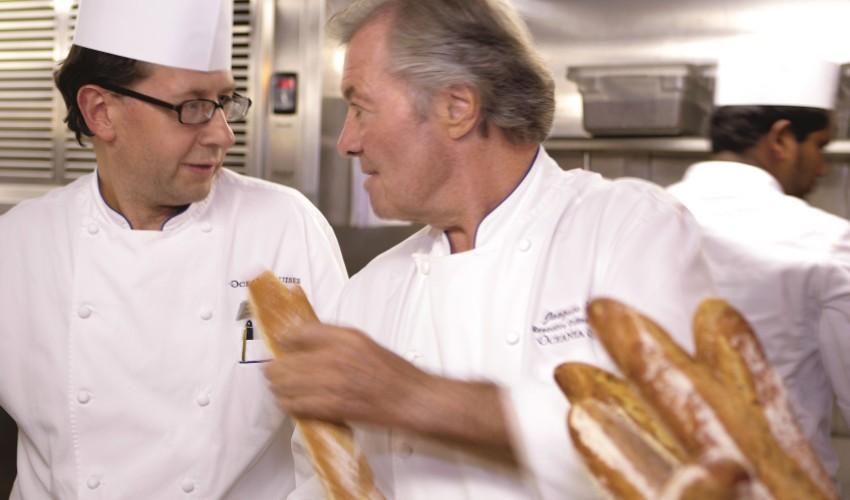 Two chefs in a kitchen talking to each other.