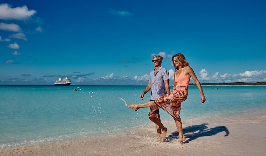 A couple walking on a beach with a cruise ship in the background.