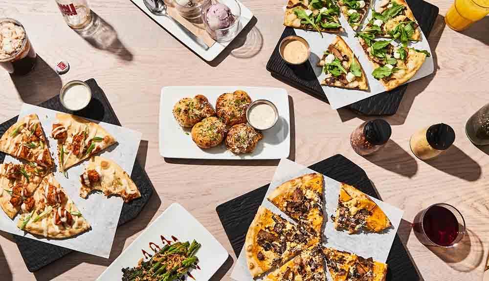 A variety of pizzas and drinks on a table.