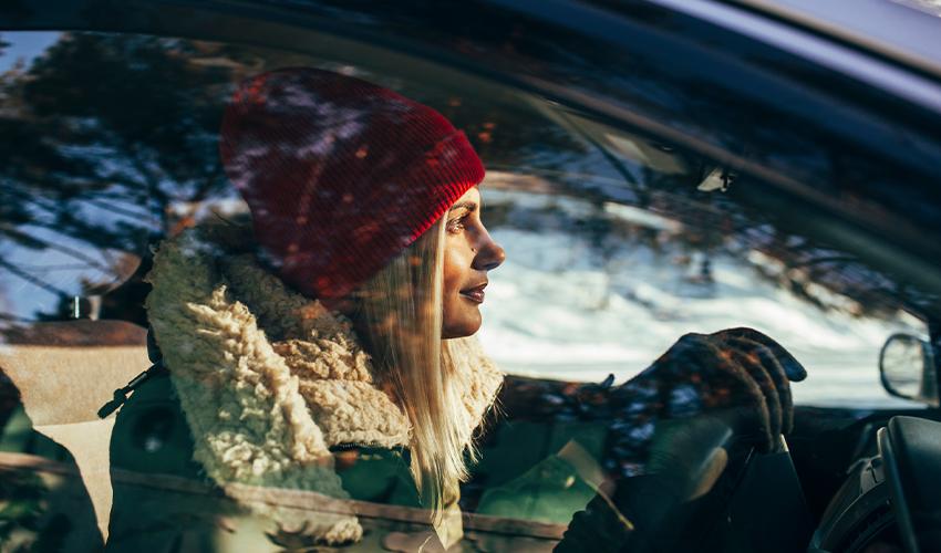 A woman in a red beanie driving a car.