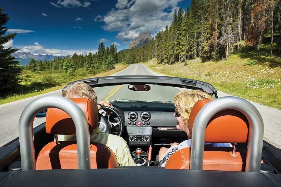 A couple in a convertible driving down a country road.