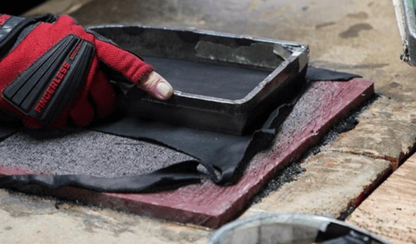 A person wearing a pair of gloves is working on a piece of wood.