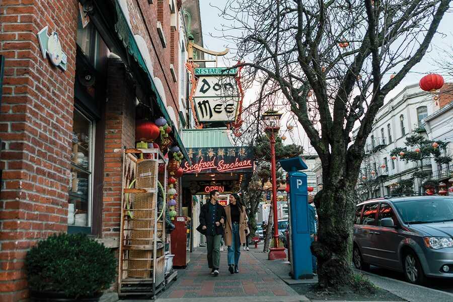 Pedestrians walking on a quaint city street with restaurants and hanging lanterns.