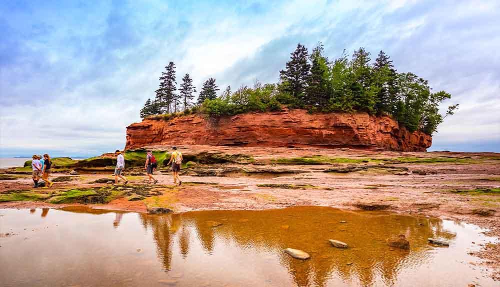 A group of people standing on a red rock in front of a pond.