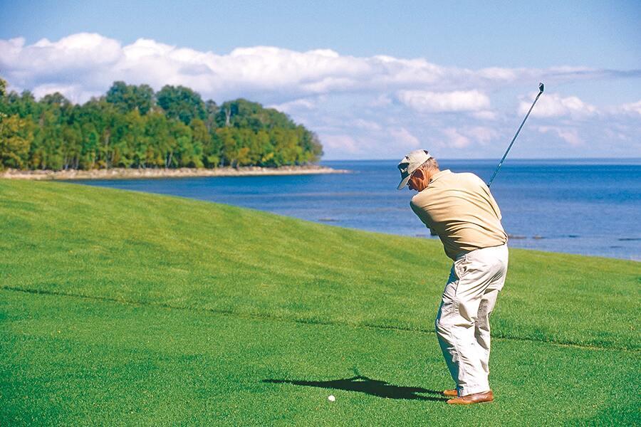 A man is playing golf on a golf course near the ocean.