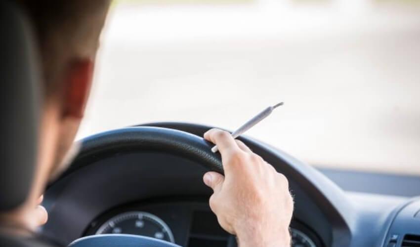 A man driving a car with a cigarette in his hand.