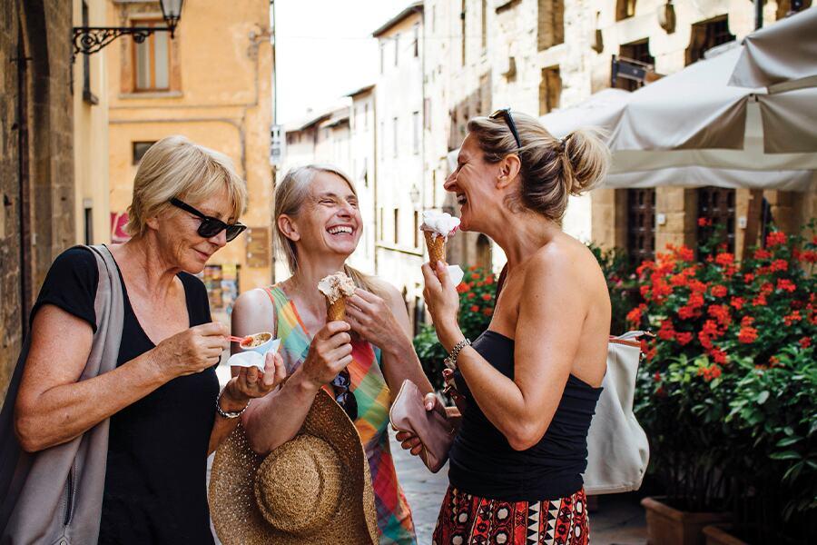 Three women eating ice cream on a street in tuscany.
