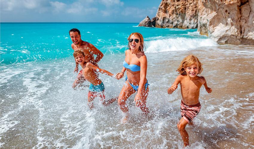 Family enjoying a playful run on a sunny beach with clear blue waters.