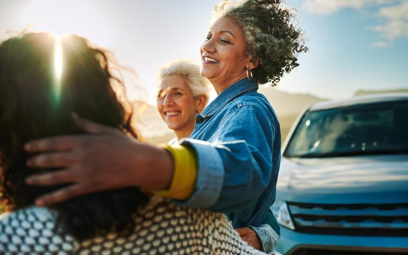 Three woman friends looking at the sun standing by a car