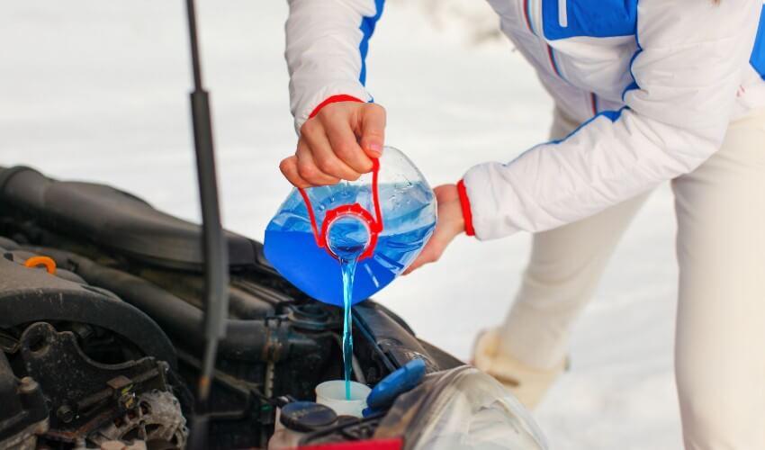 A woman pouring blue liquid into a car's hood.