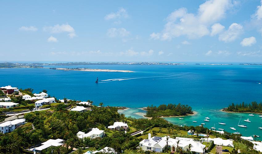 A panoramic view of a coastal region with clear blue waters, boats, and waterfront residences under a bright blue sky.
