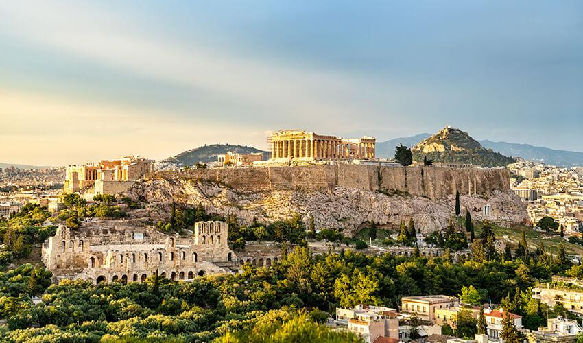 The acropolis of athens at sunset, with the parthenon and other ruins visible atop the hill.