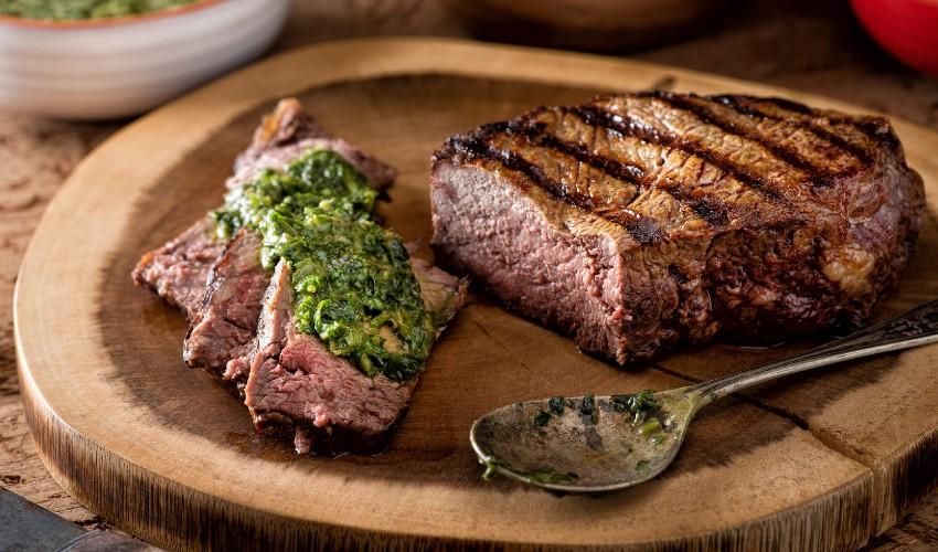 Steak with pesto on a wooden cutting board.