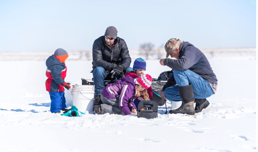 A group of people sitting in the snow with a fishing pole.