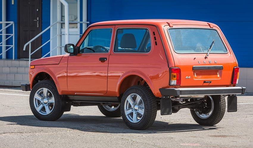 An orange suv parked in front of a blue building.