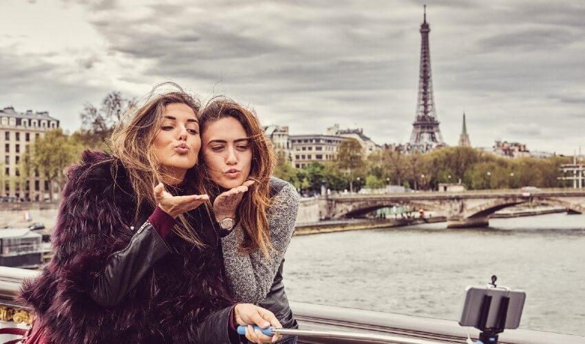 Two women are taking a selfie in front of the eiffel tower.