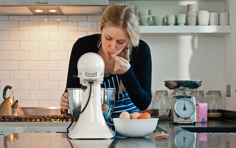 Woman in a white kitchen using a stand mixer to make a recipe.
