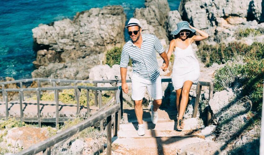 A couple walking along a rocky path near the ocean.