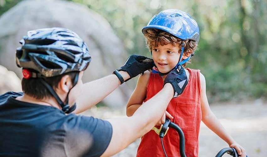 A young boy is getting his helmet adjusted by a man.